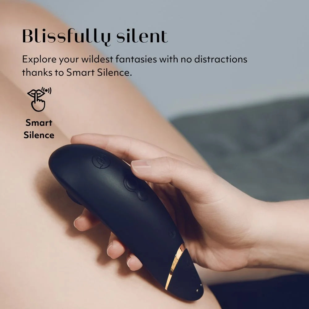 Hand holding a black clitoral stimulating vibrator with 'Smart Silence' feature, on a blurred background. 